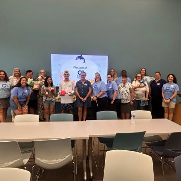 Group photo of people in a meeting room with a welcome screen.