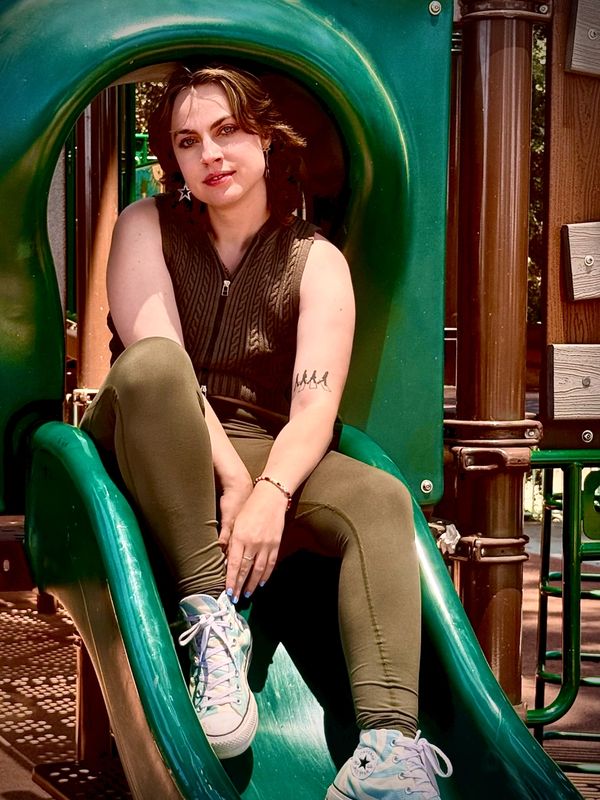 Young woman sitting on a green playground slide under sunlight.