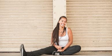 A young woman with long braids sitting on the ground, smiling.