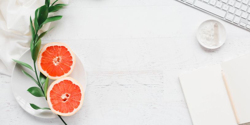 Minimalistic workspace with grapefruit halves and greenery on a white plate.