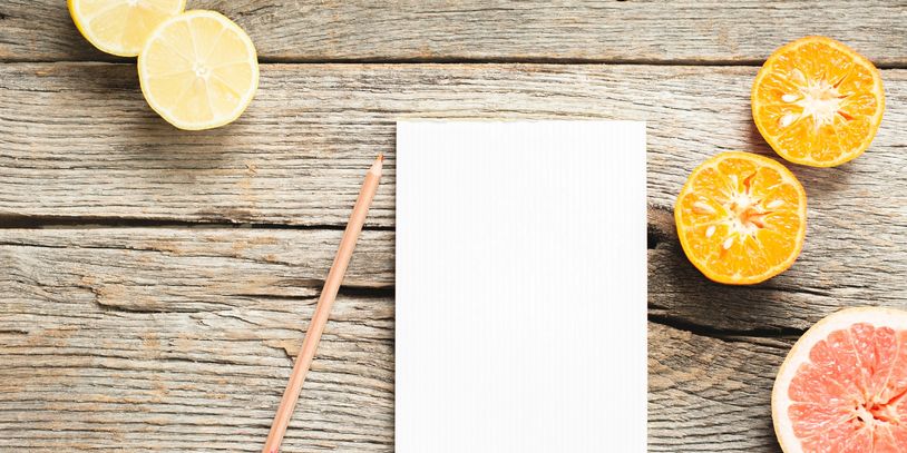 Blank notepad with pencil on wooden table surrounded by citrus fruits.