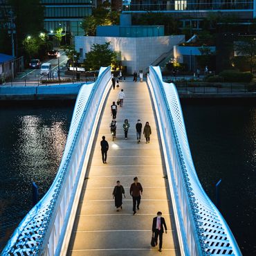 Illuminated pedestrian bridge at night with people walking across it.