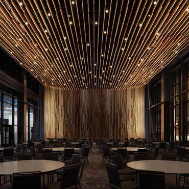 Modern event hall with round tables and wooden ceiling lights.