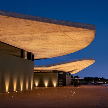 Modern building with large curved concrete roofs illuminated at night.