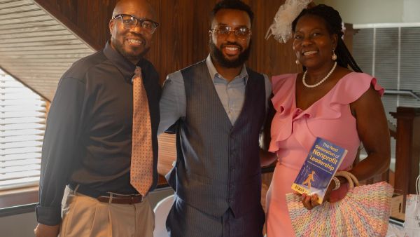 Three smiling people posing together, with one woman holding a book titled 'The Next Generation of Nonprofit Leadership.'