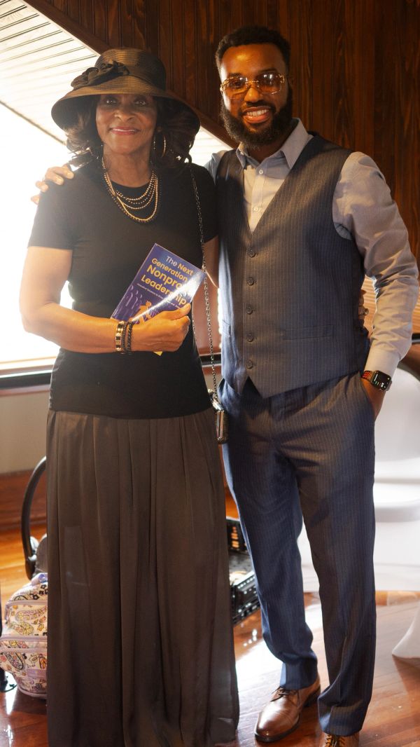 Two smiling individuals posing indoors, one holding a book titled 'The Next Generation Nonprofit Leadership'.