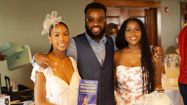 Three smiling people at an event, one holding a book on nonprofit leadership.