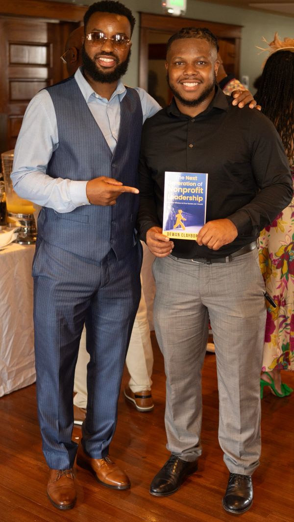 Two men smiling, one pointing at a book titled 'The Next Generation of Nonprofit Leadership'.