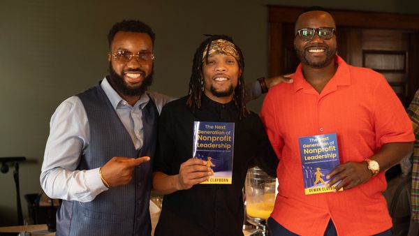 Three men smiling, holding a book titled 'The Next Generation of Nonprofit Leadership.'