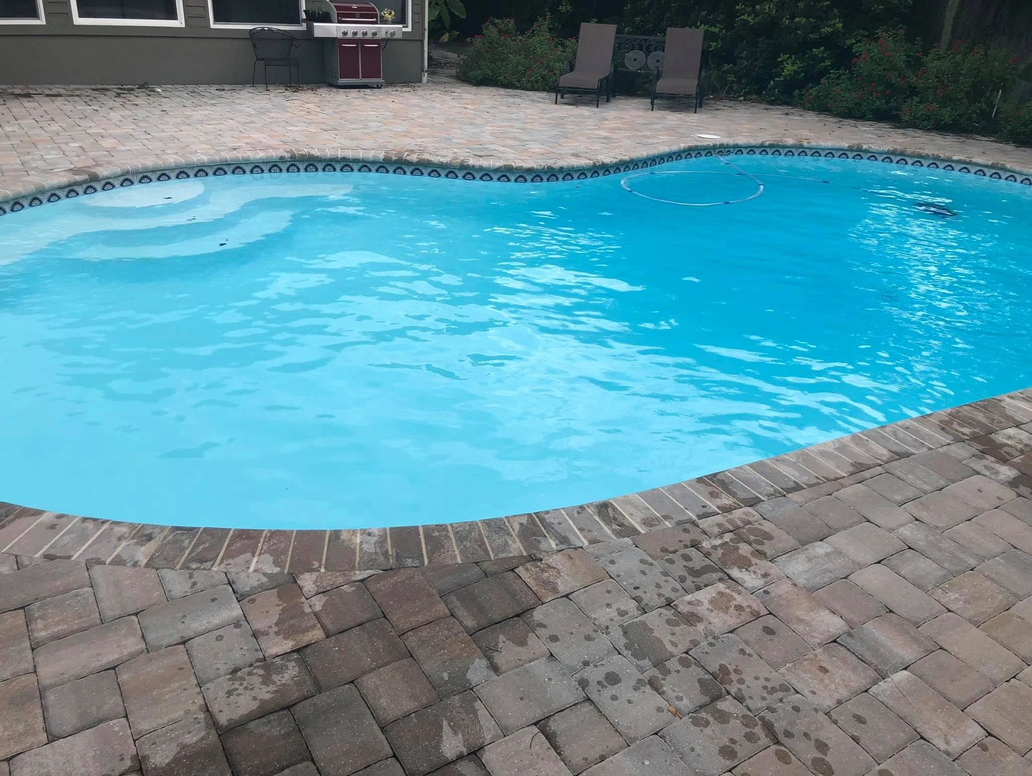 Clean backyard pool with patio chairs and a grill.