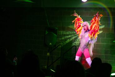 Drag queen performing under stage lights, colorful motion blur emphasizing energy and pride.