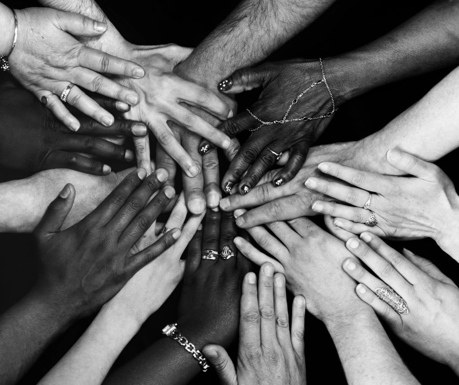 A group of people of diverse backgrounds each putting their hands together in the centre