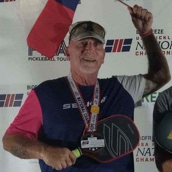 Man holding pickleball paddle and medal, celebrating victory.