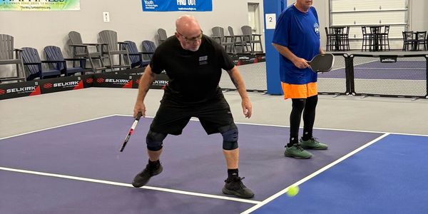 Two men playing pickleball indoors on a court, one preparing to hit the ball.
