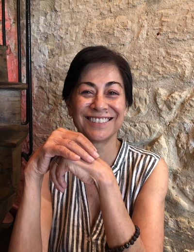 Lisa Cuizon sitting at a table smiling near a stone wall and spiral staircase in Paris