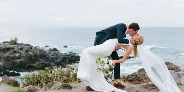 Groom dipping bride as he kisses her on the beach
