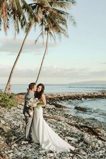 Bride and groom on a beach under palm trees as groom kisses his new wife