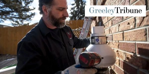 A man installs a white vent pipe on a brick wall using a power drill.