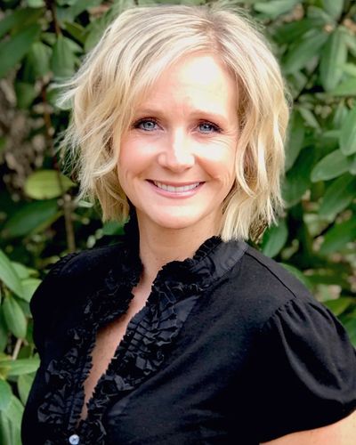 Smiling woman with short blonde hair and blue eyes in black ruffled blouse.