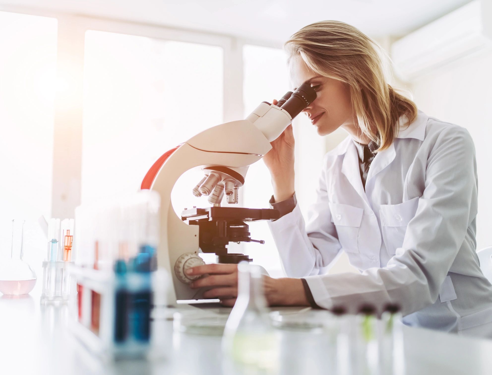 Woman Lab Technician looking into binocular compound microscope in a lab setting