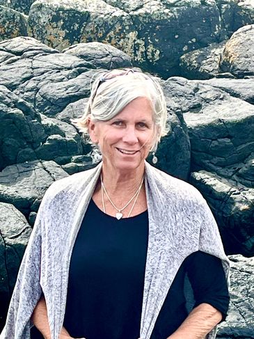 Smiling woman with short gray hair standing by rocky terrain.