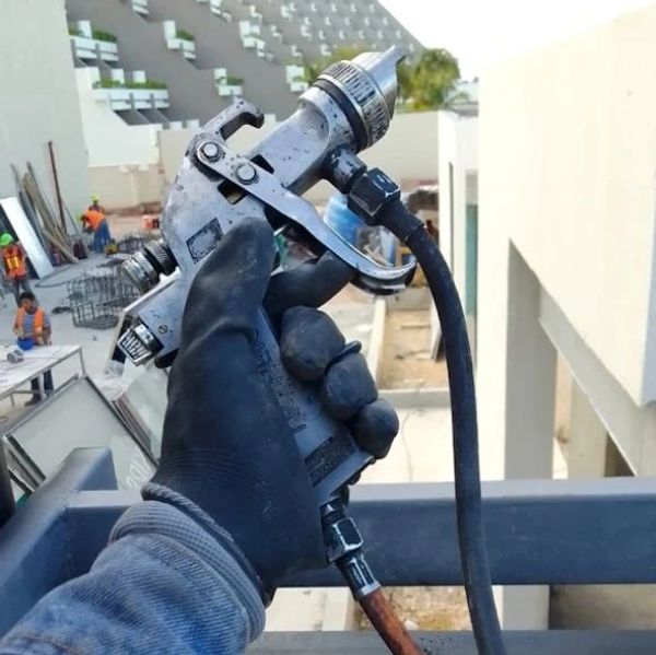 A gloved hand holding a spray gun at a construction site.