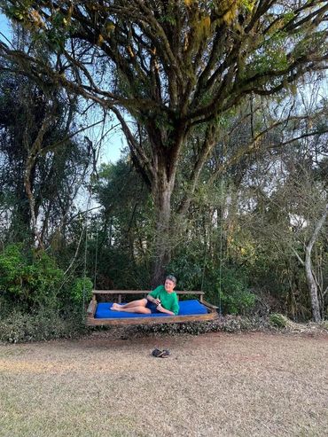 Person relaxing on a large blue cushion swing hanging from a tree in a garden.