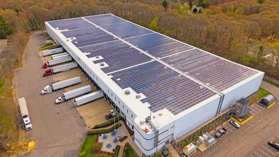 A large warehouse with solar panels on the roof and trucks parked outside.