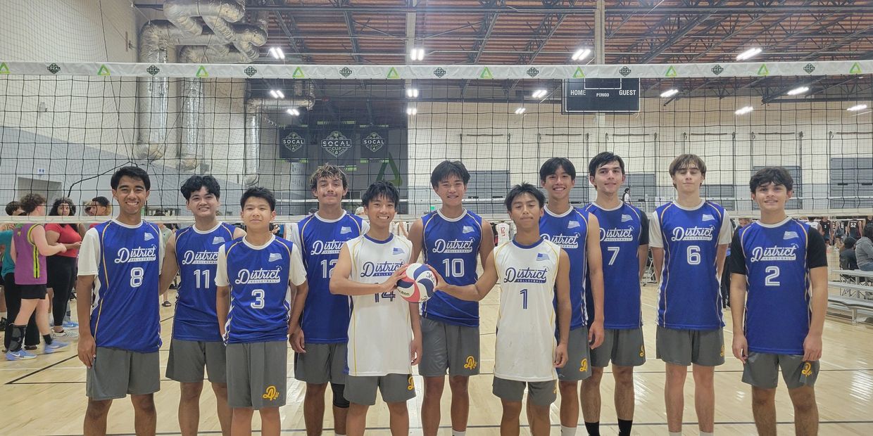 Youth volleyball team posing in gym with net behind them.
