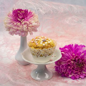 Flower cupcake on cupcake pedestal with pink mums adjacent to cupcake
