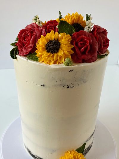 Double barrel tall cake with red roses and sunflowers on semi naked frosted cake