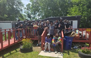 Group of people posing outdoors on a red wooden deck.