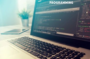 Laptop keyboard and screen displaying code in a bright workspace.