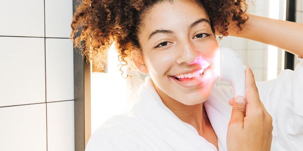 Young person holding Lightstim for acne to side of face while smiling