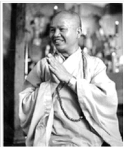 A young Vietnamese man, smiling. He is wearing monk's robes and a long beaded mala.