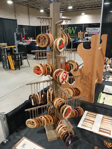Handcrafted wooden Christmas-themed keychains displayed on a rotating stand at a craft fair.