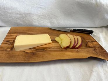 Sliced apple and a block of cheese on a wooden board with a knife.