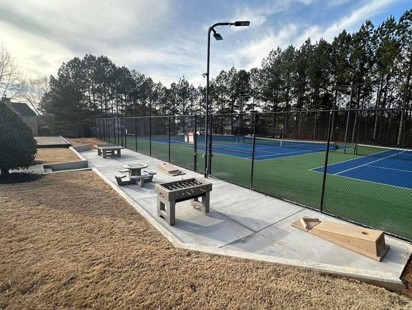 Outdoor recreational area with foosball, cornhole, and tennis courts.