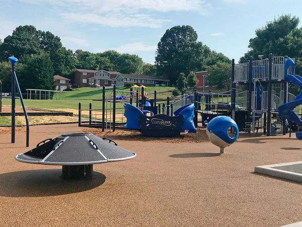 Modern playground with blue play structures and spinning equipment on a rubber surface.