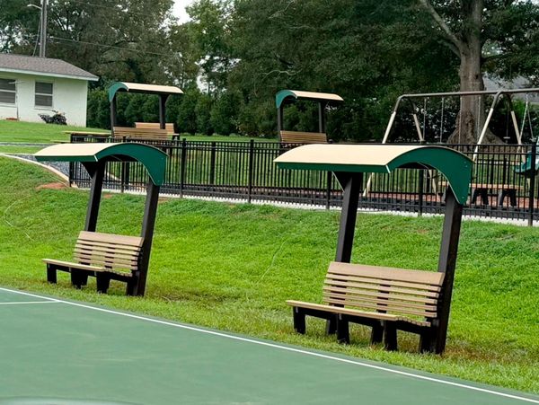 Sheltered wooden benches near a green sports court with a playground in the background.