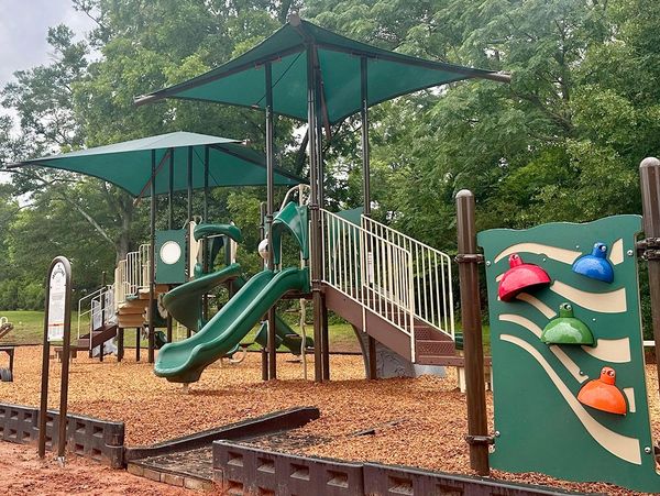 Modern playground with slides and shaded areas surrounded by trees.