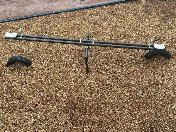 Empty seesaw on wood chip playground surface with tire supports.