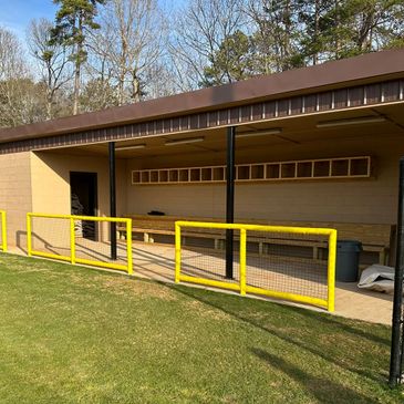 Empty baseball dugout with yellow railings and green field.