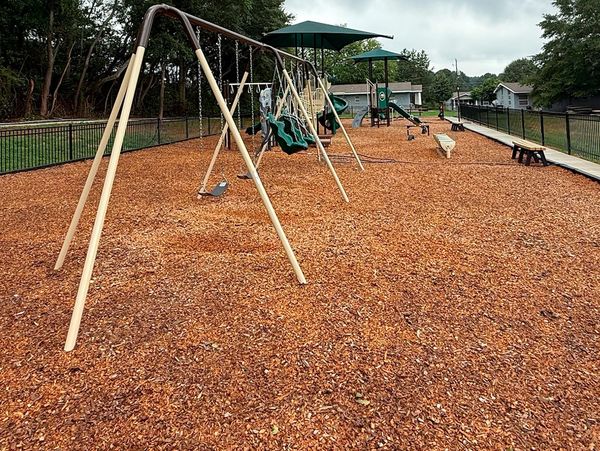 Empty playground with swings and wood chip ground covering on a cloudy day.