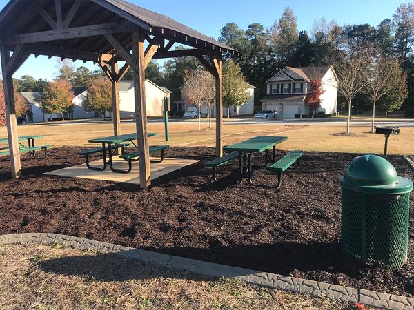 Picnic area with benches, a shelter, and a trash can in a neighborhood park.