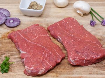 Thick-cut Braising Steak on wooden chopping board with garnish. Born & reared in Malpas.