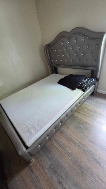 Luxurious gray tufted bed frame with mattress and pillows in a minimalist room.