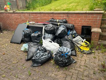 Pile of black garbage bags and garden tools against a brick wall.