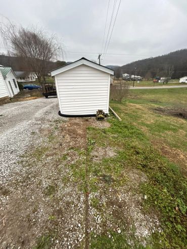 Small white shed tilting awkwardly on gravel and grass.