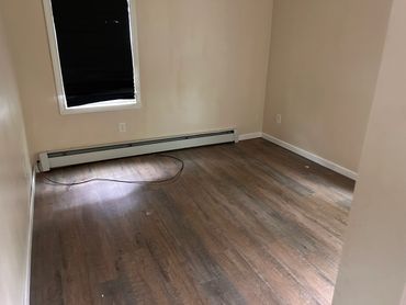 Empty room with wood flooring, beige walls, and a window with a black blind.